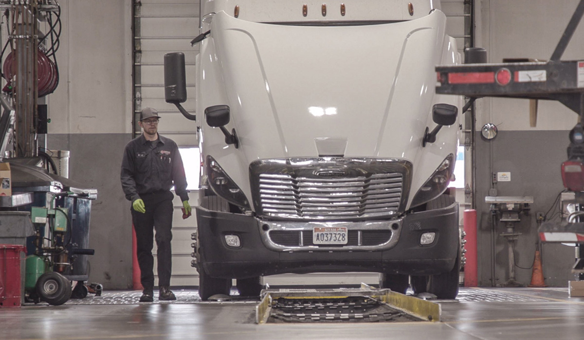 Photo of technician walking by Freightliner truck with open hood